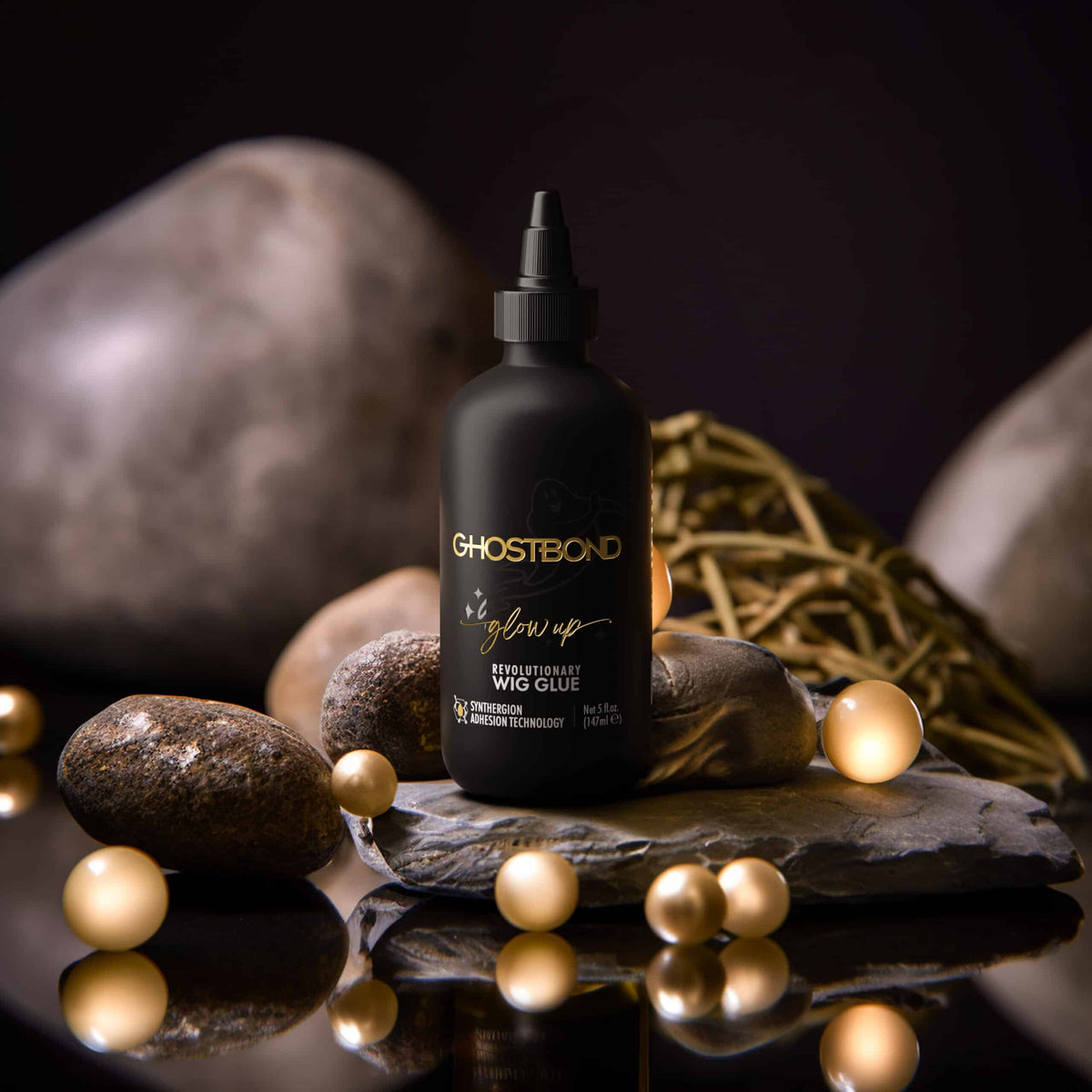 Ghostbond wig glue bottle on a dark surface with rocks and pearls