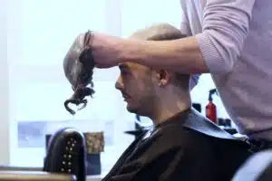 Barber fitting a customer's hair system in a salon setting.
